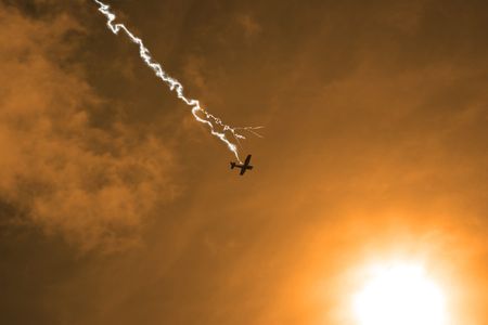 a silhouette of a light plane heading into the sunshine being hit by lightningの写真素材