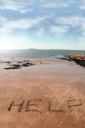 help inscribed on the beach with waves in the background on a hot sunny dayの写真素材