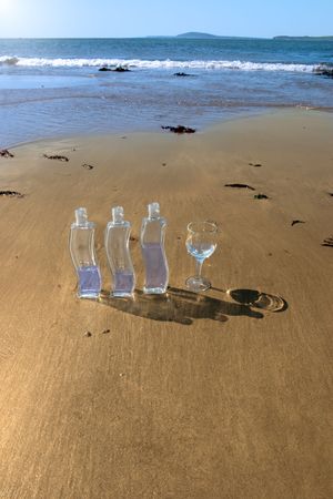three bottles and a glass of pure natural water standing on the beach in kerry irelandの写真素材