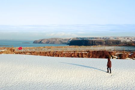 child on a snow covered golf course in ireland in winter with sea and cliffs in backgroundの写真素材