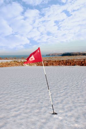 flag on a snow covered golf course in ireland in winter with sea and cliffs in backgroundの写真素材