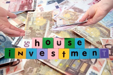 toy letters that spell house investment with cash in hands against a money background の写真素材