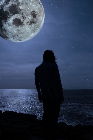 a lone woman looking sadly over the cliffs edge under the full moon in county clare irelandの写真素材