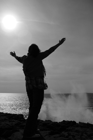 a lone woman raising her arms in awe at the powerful waves on the cliffs edge in county clare ireland in black and whiteの写真素材