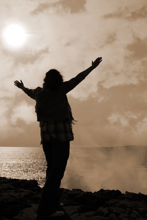 a lone woman raising her arms in awe at the powerful waves on the cliffs edge in county clare ireland in sepiaの写真素材
