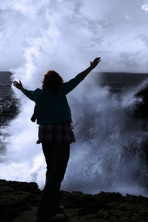 a lone woman raising her arms in awe at the powerful waves on the cliffs edge in county clare irelandの写真素材