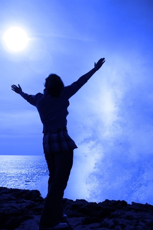 a lone woman raising her arms in awe at the powerful wave on the cliffs edge in county clare irelandの写真素材