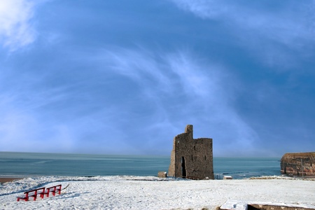 a seasonal snow covered view of atlantic ocean and ballybunion castle with red benches on a frosty snow covered winters dayの写真素材