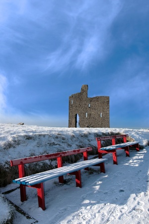 a seasonal snow covered view of atlantic ocean and ballybunion castle with red benches on a frosty snow covered winters dayの写真素材