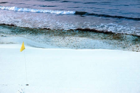 a snow covered links golf hole in ireland in winter weather with yellow flagの写真素材