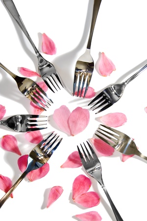 forks surrounding a heart shape petal with rose petals for a concept on romantic dining on white backgroundの写真素材