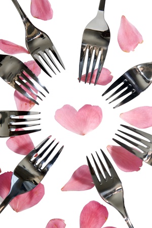 forks surrounding a heart shape petal with rose petals for a concept on romantic dining on white background with clipping pathの写真素材
