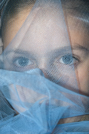 a beautiful young girl staring out from beneath a blue veilの写真素材