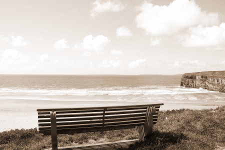 Beautiful view over the Ballybunion beach and cliffs in Ireland from a wooden bench in sepiaの写真素材