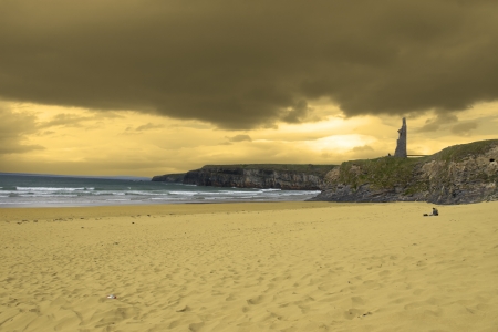 couple meditating on a golden beach in Ireland with castle in background in sepiaの写真素材