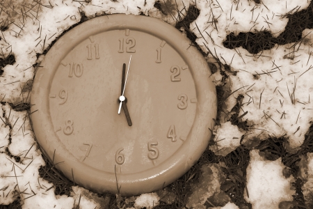 a clock face in the snow covered grass as if frozen in time in sepiaの写真素材
