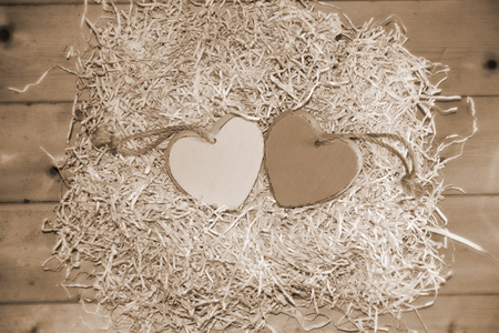 two wooden hearts in a love nest made of straw on a wooden background in sepiaの写真素材