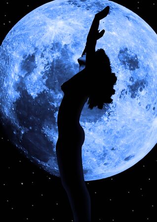 attractive silhouetted nude woman holding her hands up to the moon giving gratitude to the heavens in a yoga pose with a cloudy backgroundの写真素材