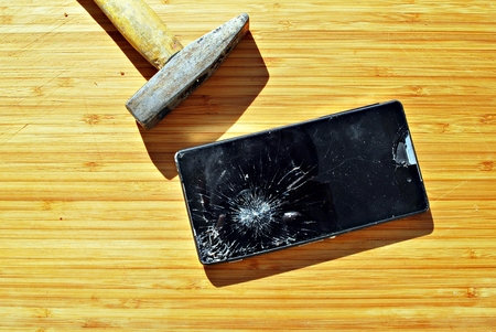 Smashed phone screen on a table with a hammerの写真素材