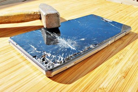 Smashed phone screen on a table with a hammerの写真素材