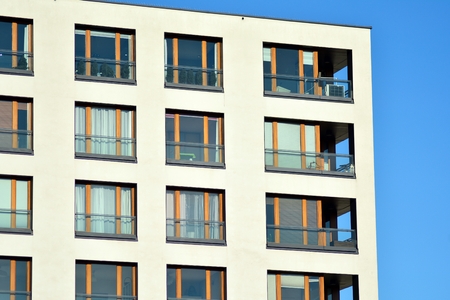 Fragment of a building with windows and balconies. Modern home with many flats.