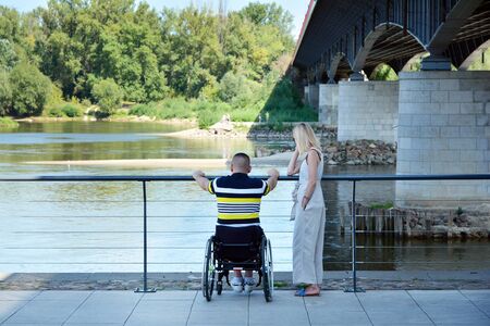 View of active woman interacting with disabled man on a promenade an river.の写真素材