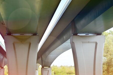 Bottom view of a huge flyover motorway, blue sky, large pillars.