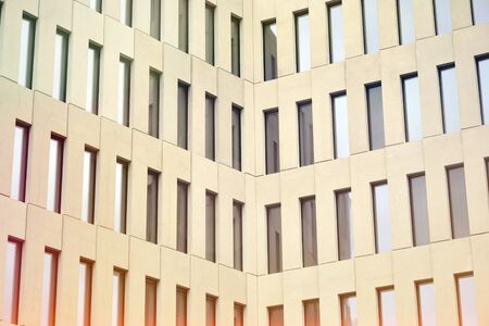 Modern office building detail. Perspective view of geometric angular concrete windows on the facade of a modernist brutalist style building surface with sunlight.の写真素材
