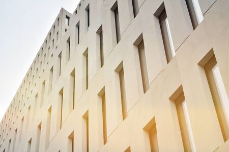 Modern office building detail. Perspective view of geometric angular concrete windows on the facade of a modernist brutalist style building surface with sunlight.の写真素材