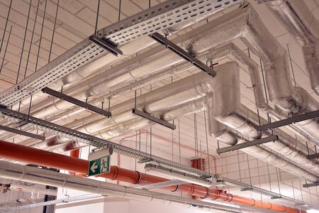 Water pipes and cable trays run under ceiling of a buildingの写真素材