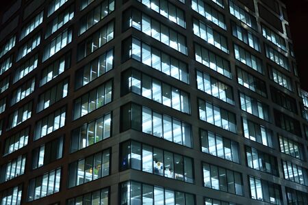 Pattern of office buildings windows illuminated at night. Lighting with Glass architecture facade design with reflection in urban city.の写真素材