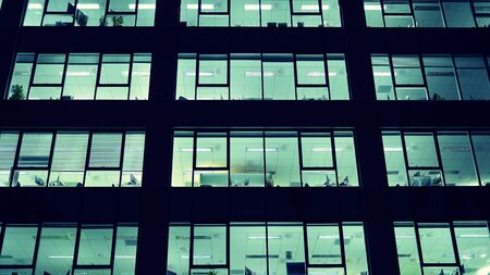 Pattern of office buildings windows illuminated at night. Lighting with Glass architecture facade design with reflection in urban city.の写真素材