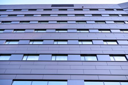A view at a straight facade of a modern building with a dark gray facade. Dark gray metallic panel...