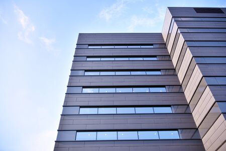 A view at a straight facade of a modern building with a dark gray facade. Dark gray metallic panel...
