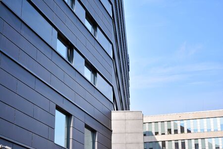 A view at a straight facade of a modern building with a dark gray facade. Dark gray metallic panel...