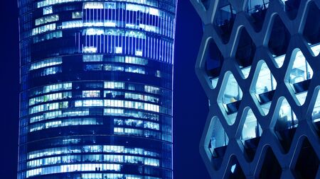 Night architecture - building with glass facade. Blue color of night lights. Modern building in business district. Concept of economics, financial.の写真素材