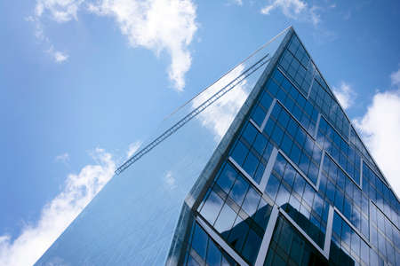 Modern curtain wall made of glass and steel. Blue sky and clouds reflected in windows of modern...