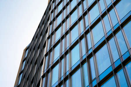 Modern curtain wall made of glass and steel. Blue sky and clouds reflected in windows of modern office building.のeditorial素材