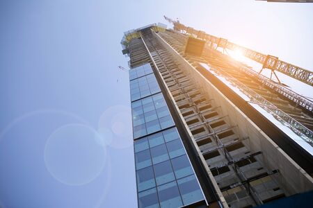 Building under construction and cranes under a cloudy sky. Modern architecture with sun ray.