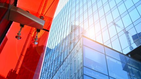 Bottom view of office building window close up with sunrise, reflection and perspective. Modern architecture with sun ray. Glass facade on a bright sunny day with sunbeams on the blue sky.の写真素材