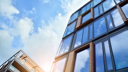 Bottom view of office building window close up with sunrise, reflection and perspective. Modern architecture with sun ray. Glass facade on a bright sunny day with sunbeams on the blue sky.の写真素材