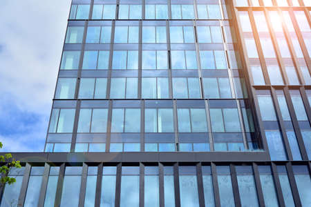 Facade texture of a glass mirrored office building. Fragment of the facade. Bottom view of modern skyscrapers in business district in evening light at sunset with lens flare filter effect.のeditorial素材