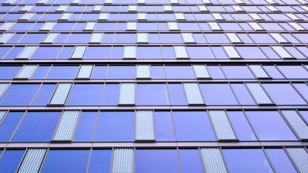 Blue curtain wall made of toned glass and steel constructions under blue sky. A fragment of a...