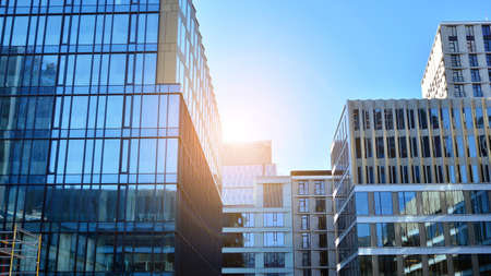 Blue curtain wall made of toned glass and steel constructions under blue sky. A fragment of a building. Glass facades on a bright sunny day with sunbeams in the blue sky.の写真素材