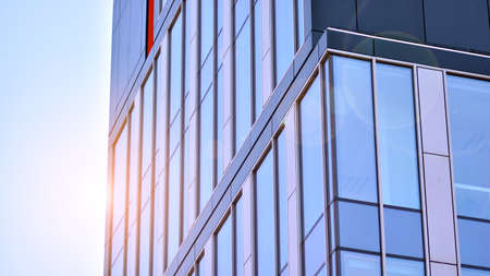 Blue sky reflection in glass facade of building. View of office building windows close up with sunrise, reflection and perspective .. Glass facade on a bright sunny day with sunbeams on the blue sky.の写真素材