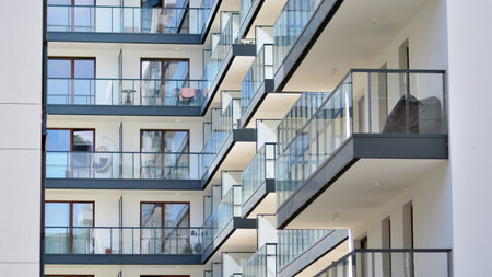 A fragment of modern architecture, walls and glass. Windows and balconies of a residential building against a blue sky. Detail of New luxury house and home complex.の写真素材