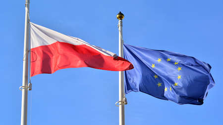 The flags of Poland and the European Union waving against the blue sky