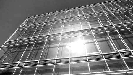 Modern office building with glass facade on a clear sky background. Transparent glass wall of office building. Bright sunny day with sunbeams on the sky. Black and white.の写真素材