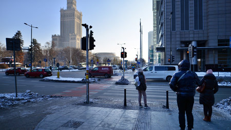 Warsaw, Poland. 14 December 2022. Winter street of a big city. People of different ages crossing the road through. View of a city street with residents, tourists and modern buildinのeditorial素材