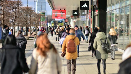 Warsaw, Poland. 8 March 2023. Crowd of people walking down an urban sidewalk with bright glowing sunlight in the background on a busy street in downtown.のeditorial素材